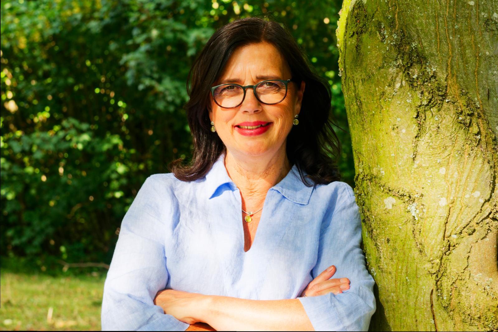 Manuela Simon, lächelnd an einen Baum gelehnt