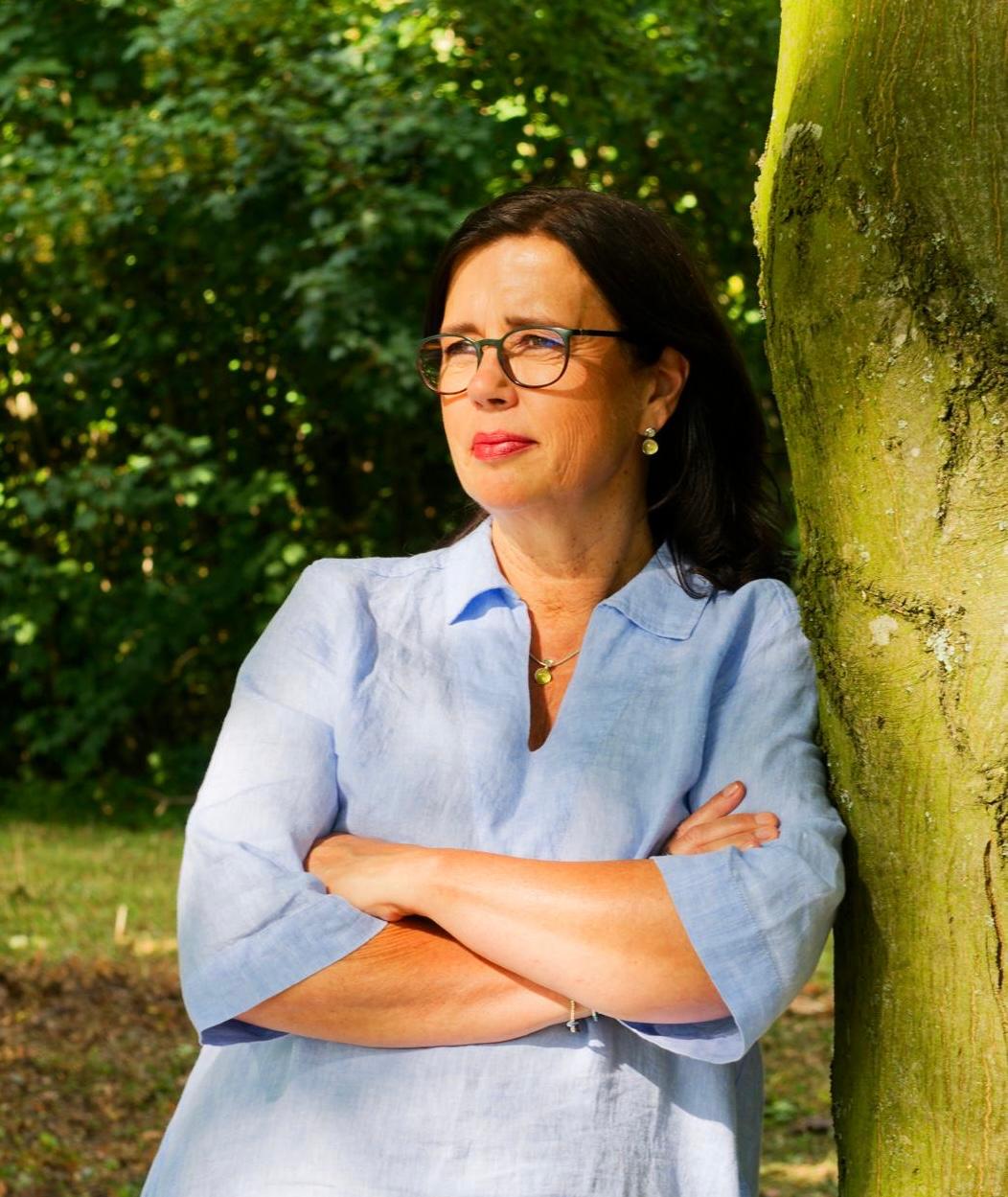 Manuela Simon an einen Baum gelehnt, nachdenklich in die Ferne blickend